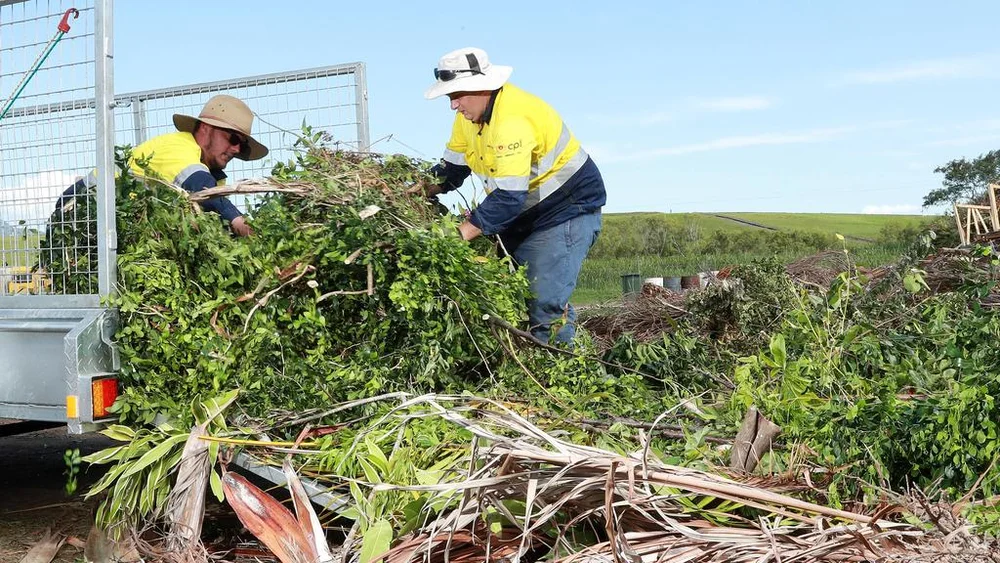 Workers loading green garden waste into a trailer